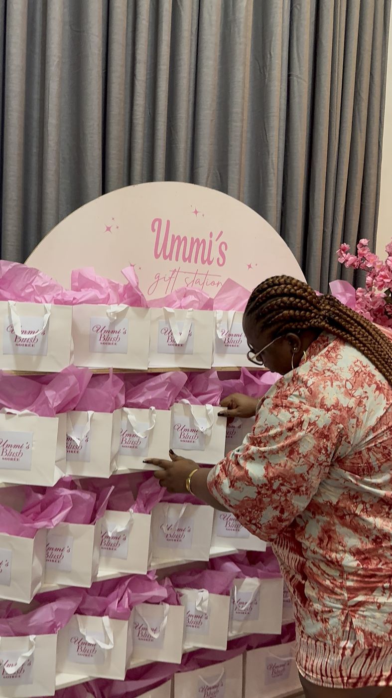 Fabsurprise team member arranging branded gift bags on a pink gift station wall