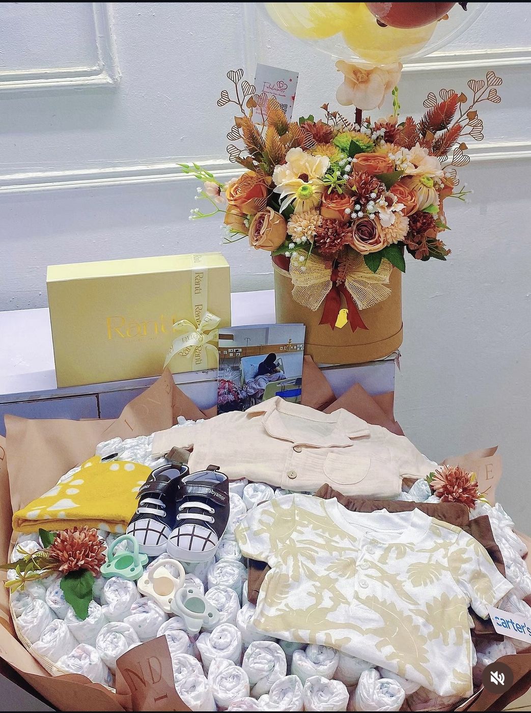 Baby shower gift bundle with a diaper cake, florals, baby clothes and shoes